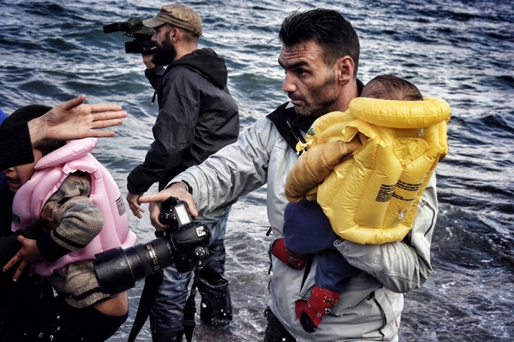 Một tay cầm máy chụp hình, một tay bồng em bé, Aris Messinis làm hai nhiệm vụ: thông tin và giúp đỡ. Hình: © Petros Tsakmakis